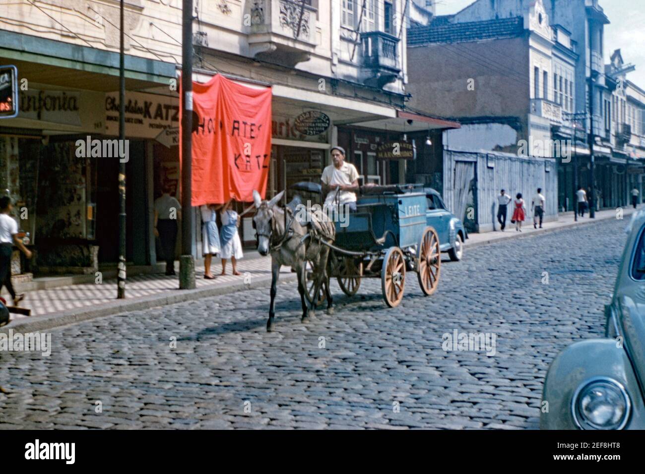 Milk being delivered by a cart being pulled by a donkey on a cobbled street in Petrópolis (also known as The Imperial City), Brazil 1961. It was common for many fresh goods were delivered door to door by carts pulled by animals or by motorised vehicles. On the side of the cart is the word ‘Leite’ – Portuguese for milk. The city of Petrópolis is located 68 km (42 ml) north east of Rio de Janeiro. It is the largest and most populous city in the Fluminense Mountain Region. This image is from an old amateur 35mm colour transparency. Stock Photo