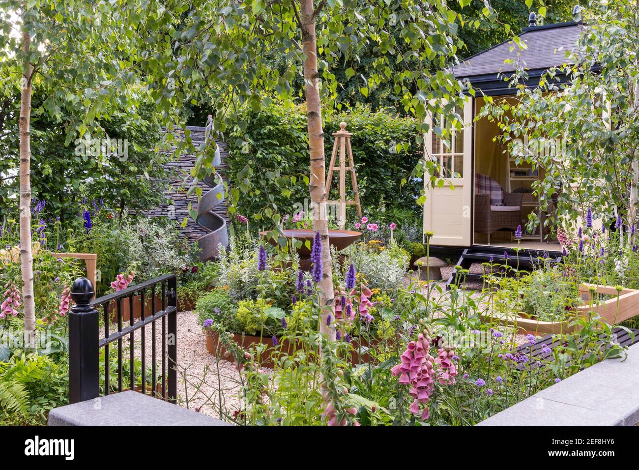 A small English cottage garden with Summerhouse Shepherds Hut in gravel garden - working from home office - raised bed flower border - London UK Stock Photo