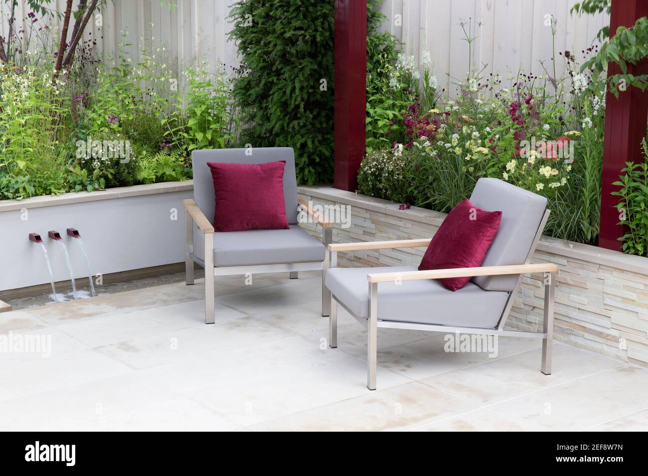 Modern urban stone garden patio with garden furniture chairs with red cushions - raised bed beds garden flower border - Summer - London UK England Stock Photo
