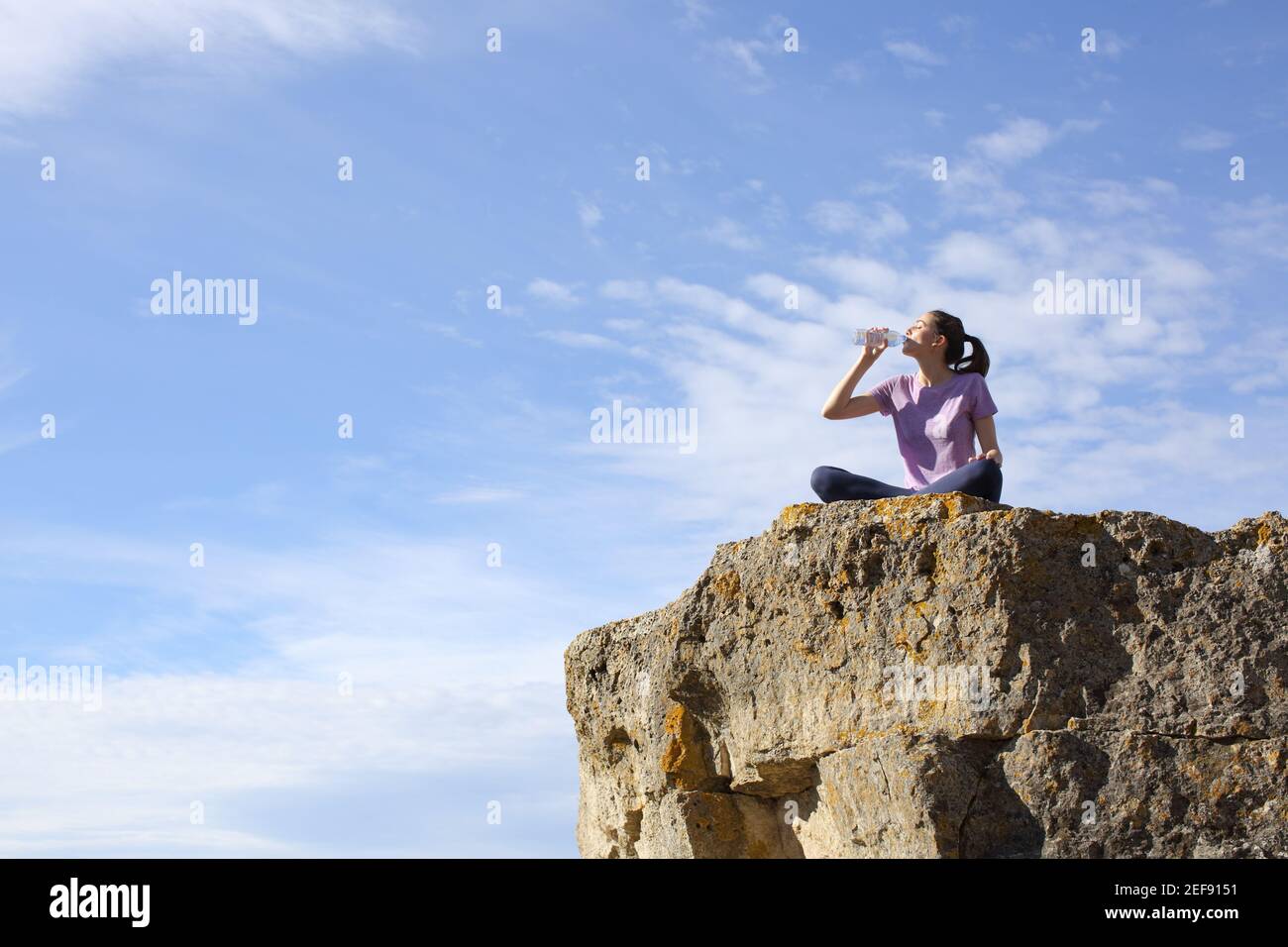 Yogi drinking water from plastic bottle after yoga exercises in the top of a cliff in the mountain Stock Photo