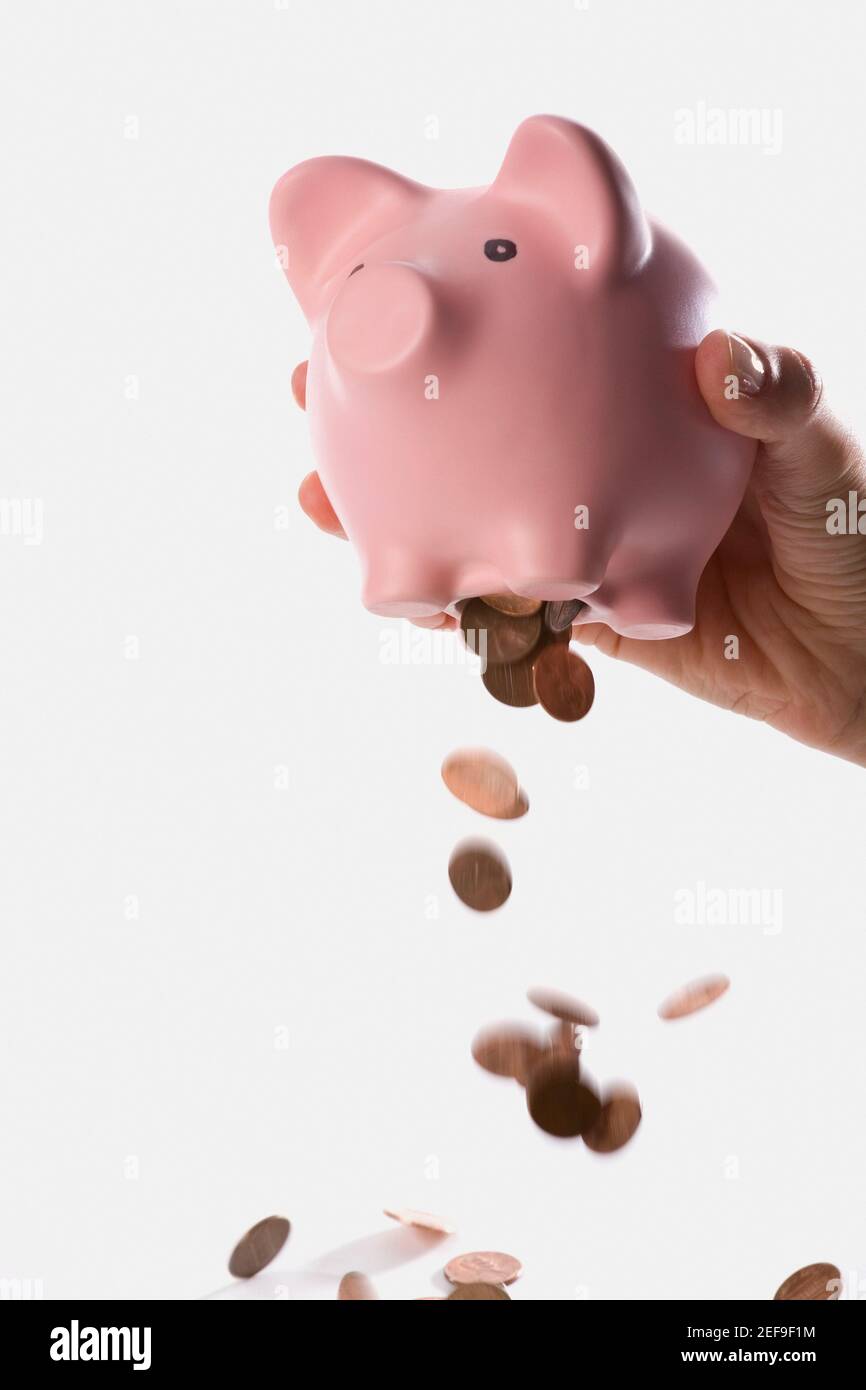 Close-up of a person dropping coins from a piggy bank Stock Photo