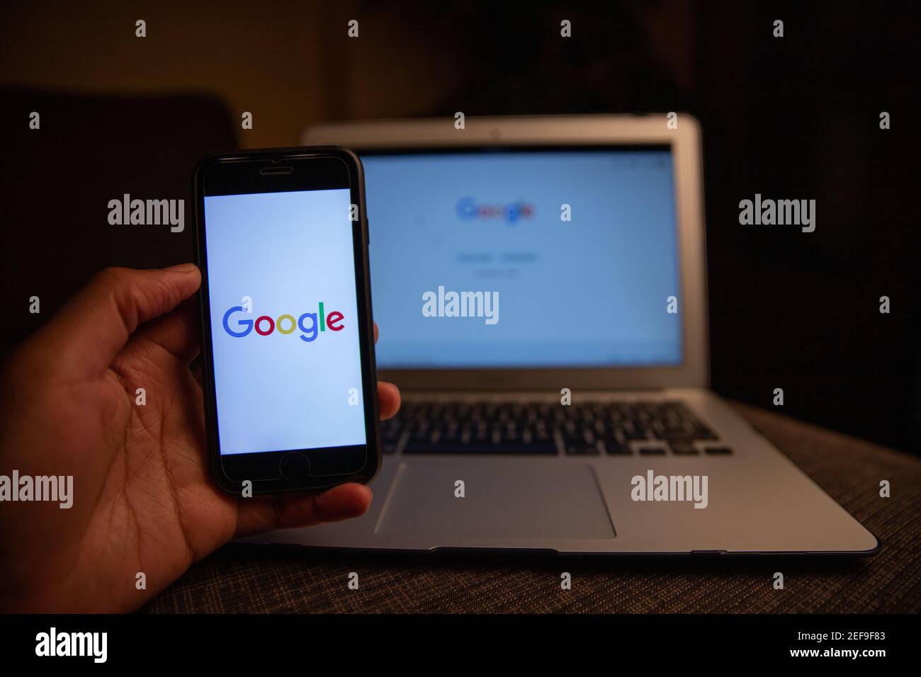 Close up of Google Logo on the iPhone display stands in front of a macbook with the desktop version.Google's the most used search engine in the world Stock Photo