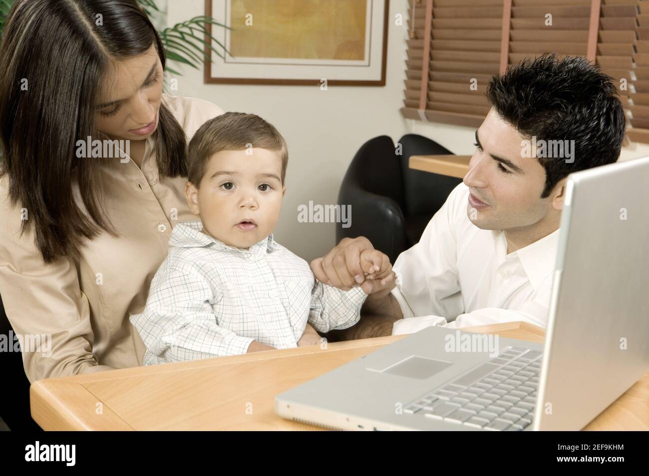 Portrait of a baby boy sitting in front of a laptop with his parents Stock Photo