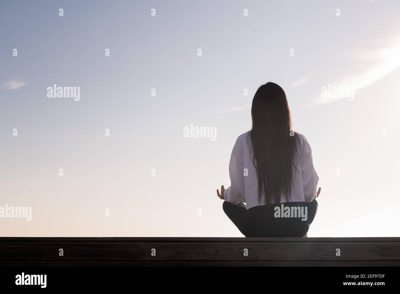 rear view of a young woman with long hair meditating at sunrise ...