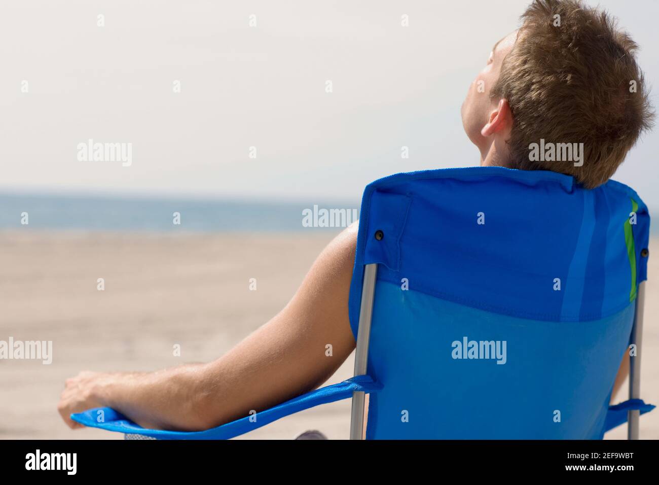 Rear view of a young man sitting on the beach Stock Photo - Alamy