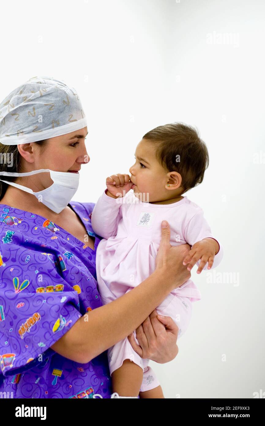 Side profile of a female doctor holding a baby girl sucking her thumb Stock Photo