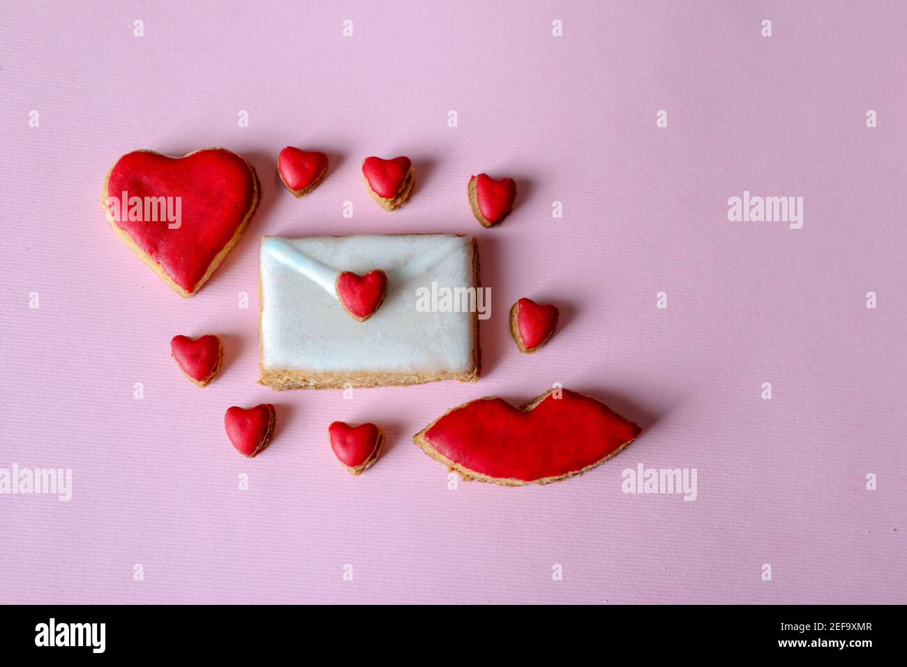 Cookies in the shape of a love letter and around it small hearts and lips isolated on purple background with copy space for text or design Stock Photo