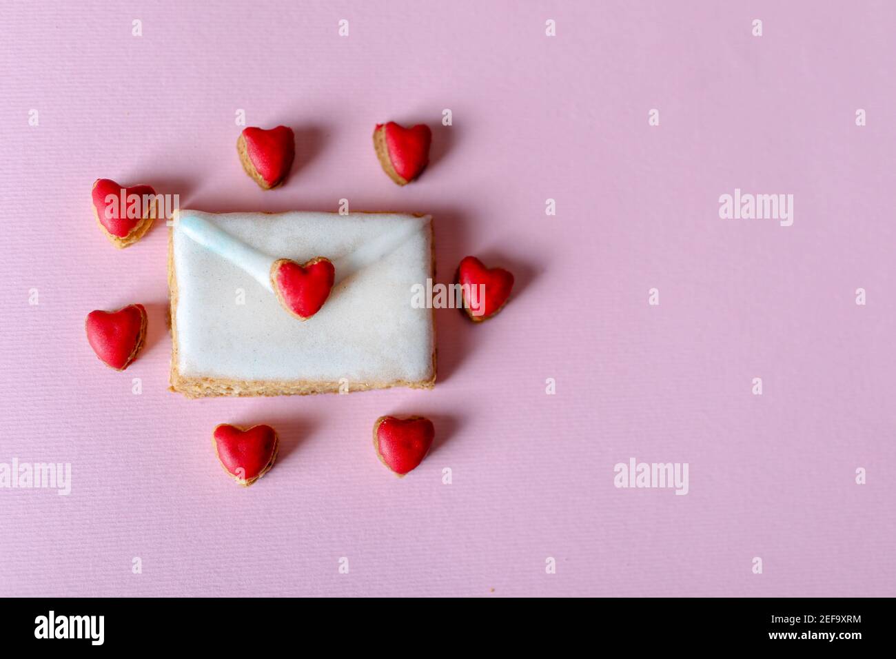 Homemade cookies in the shape of a love letter and around it small hearts isolated on purple background with copy space for text or design Stock Photo