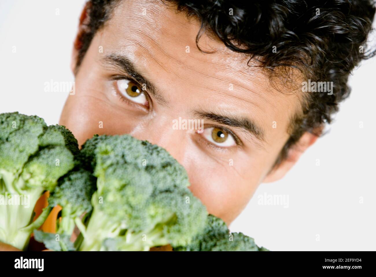 Portrait of a young man holding broccoli in front of his face Stock Photo