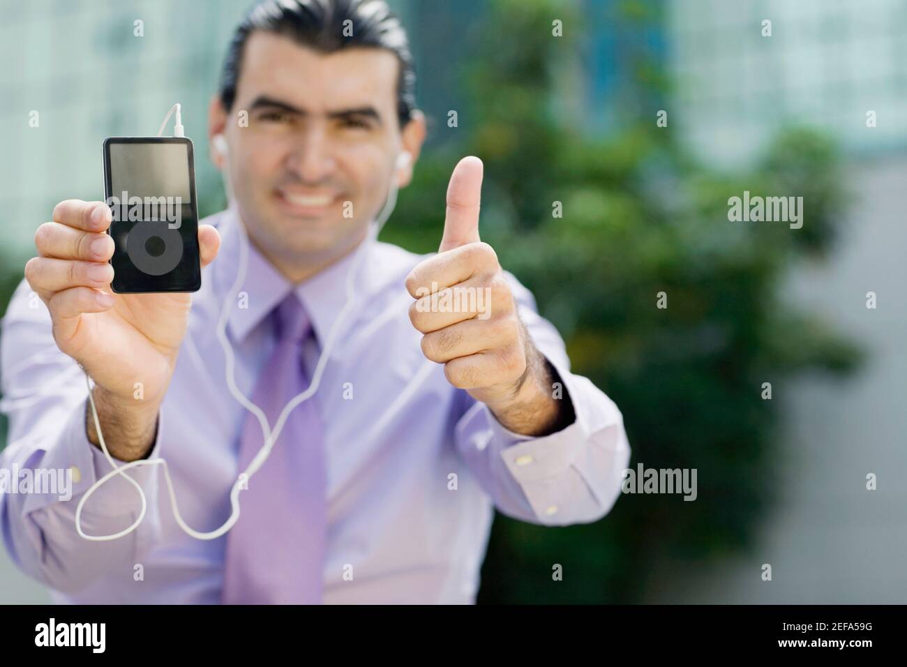 Portrait of a businessman showing an MP3 player and making a thumbs up