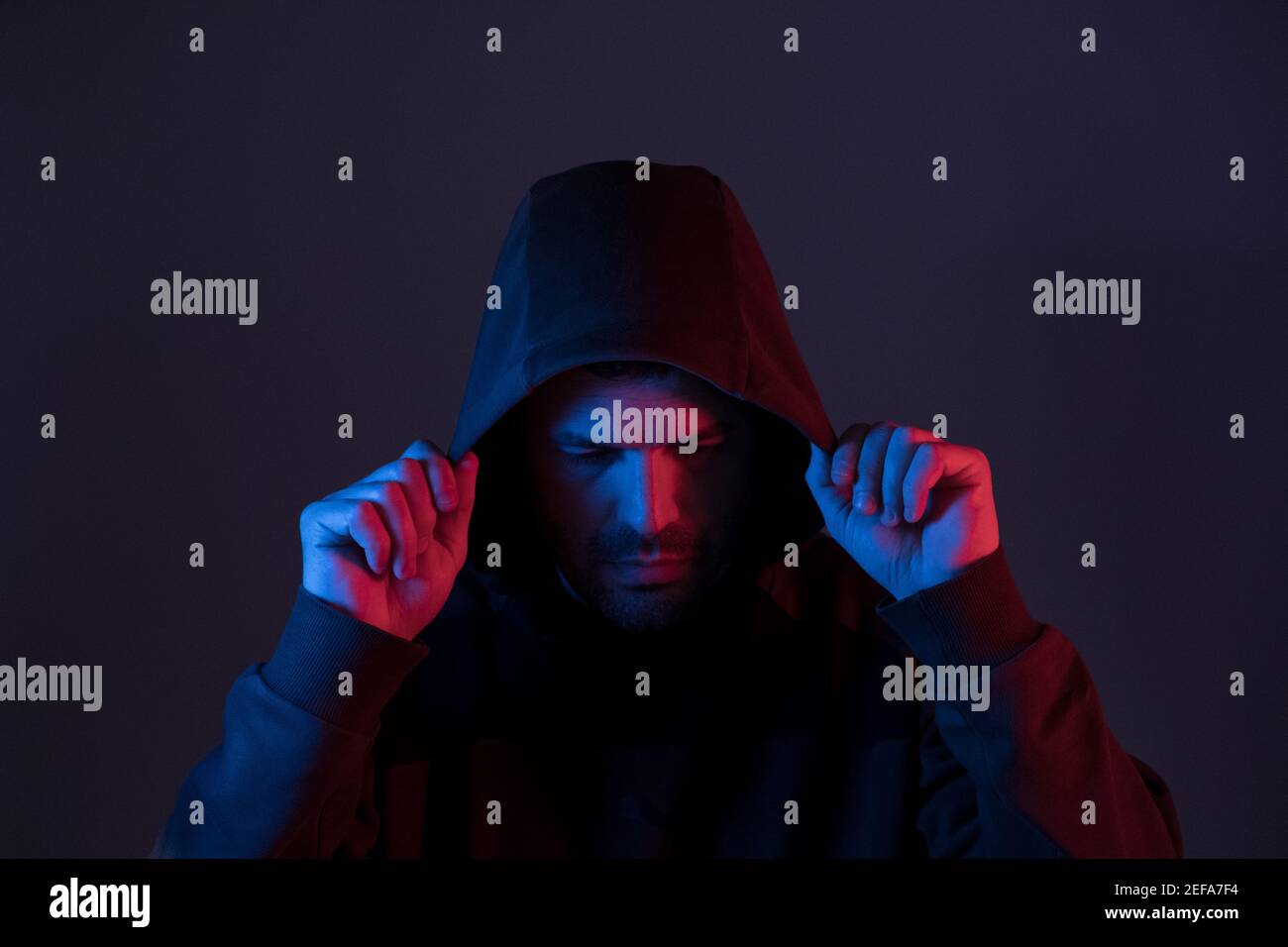 a man illuminated with colored neon lights puts on a hoodie Stock Photo