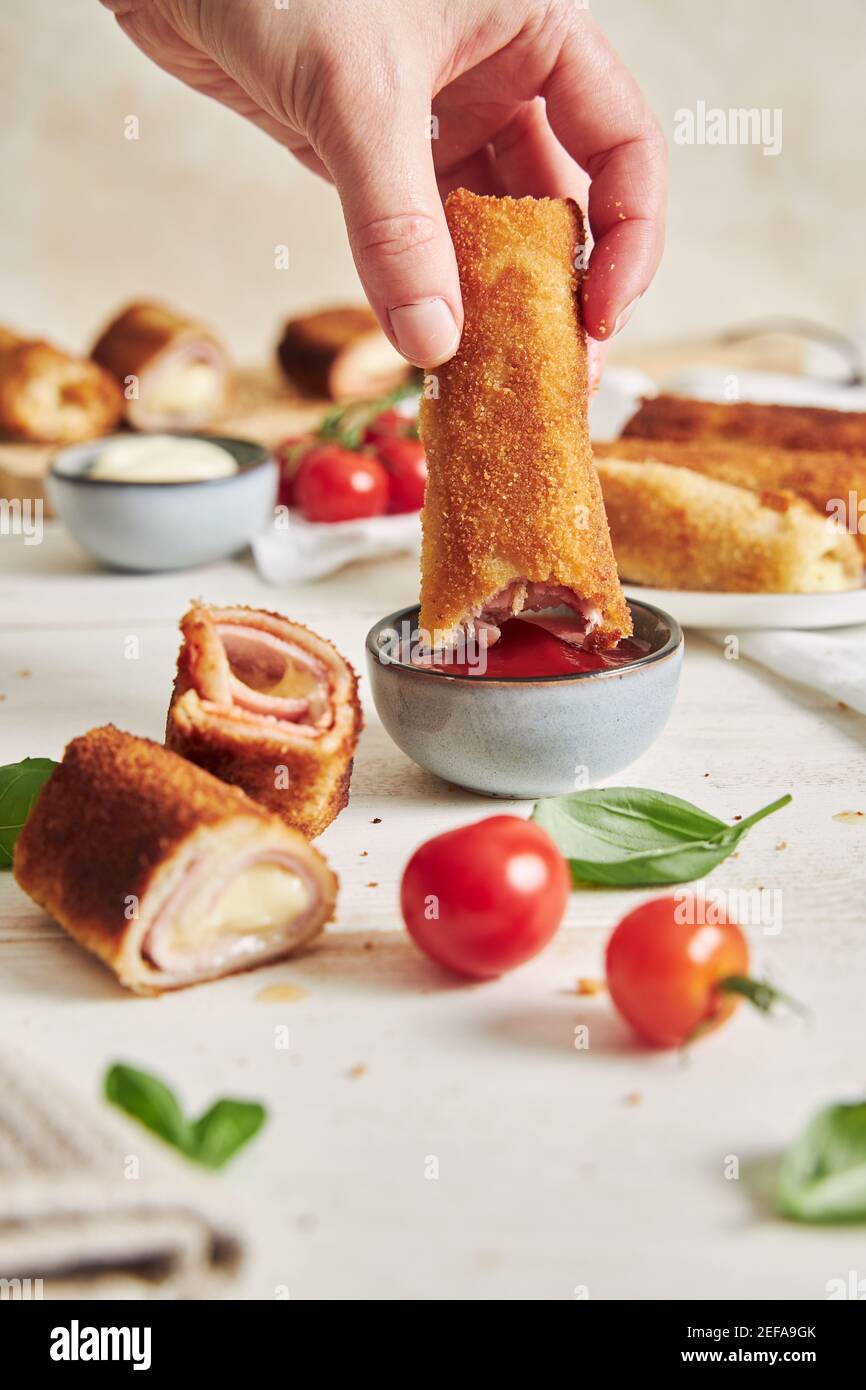 Vertical shot of a person dipping ham and cheese toast roll in tomato