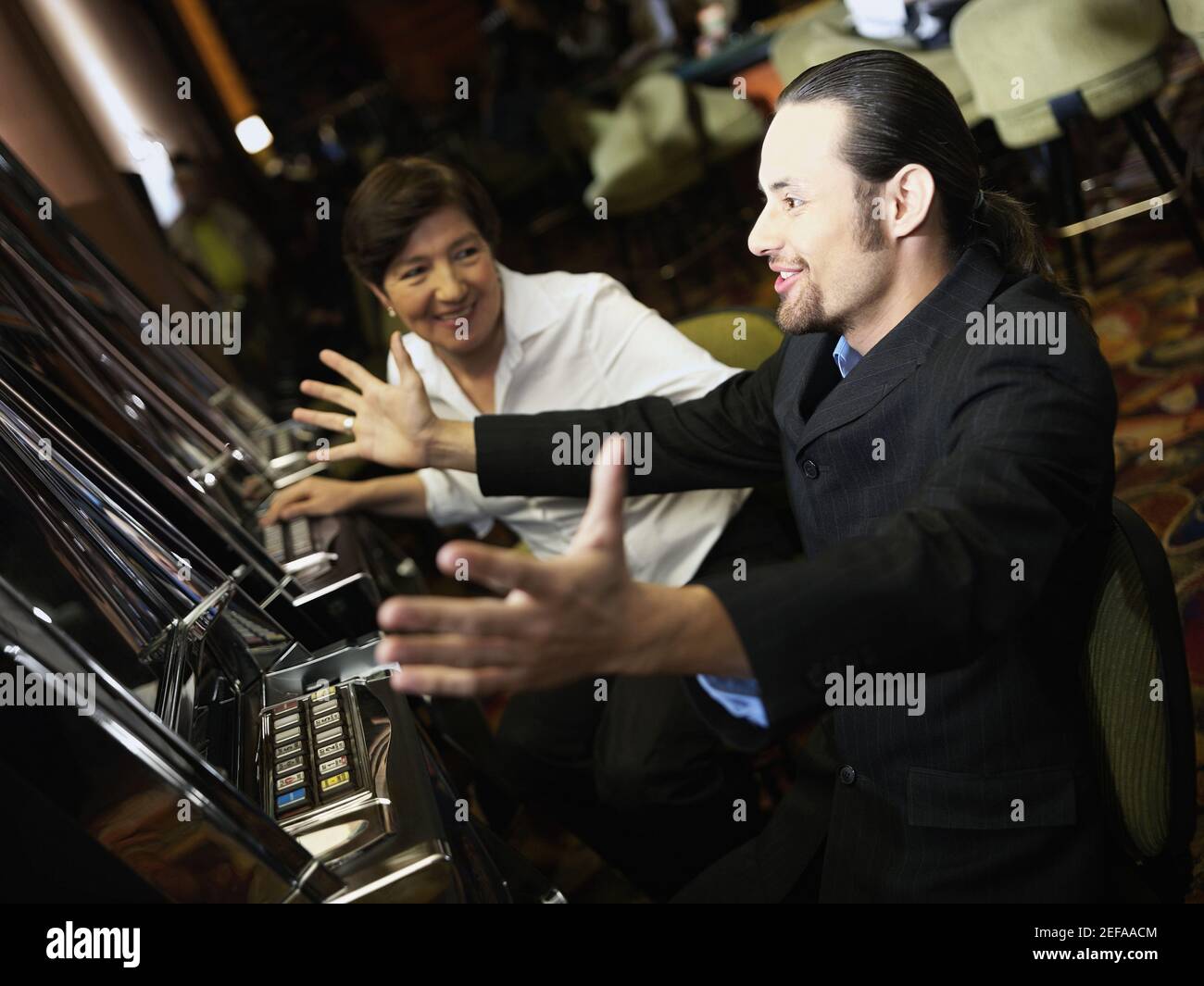 Mid adult man cheering in front of a slot machine with a mature woman smiling beside him Stock Photo