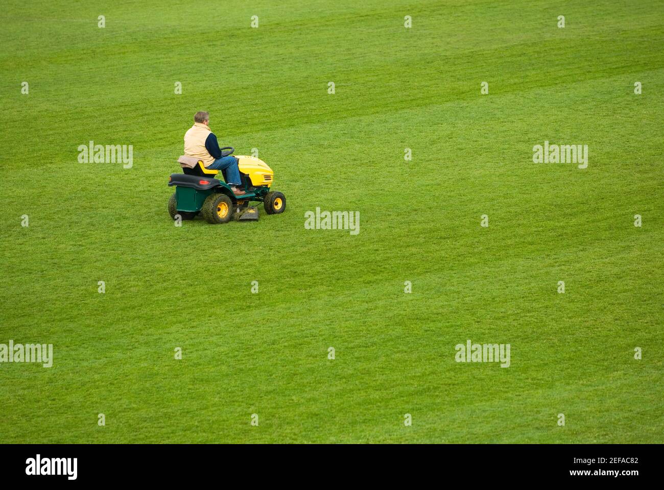 Side profile of a man mowing grass with a lawn mower in a field Stock Photo