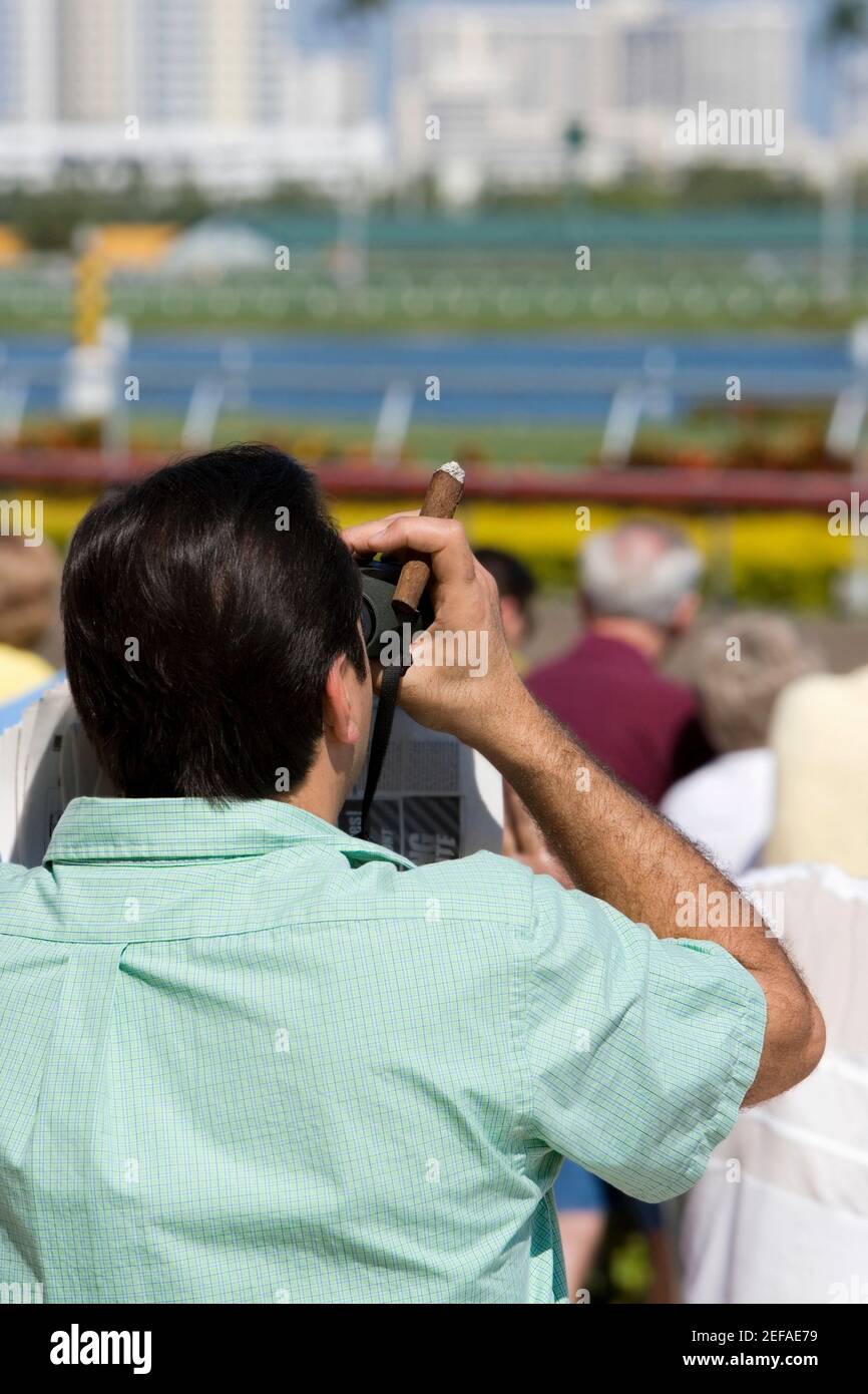 Rear view of a spectator looking through a pair of binoculars at the horseracing track Stock Photo
