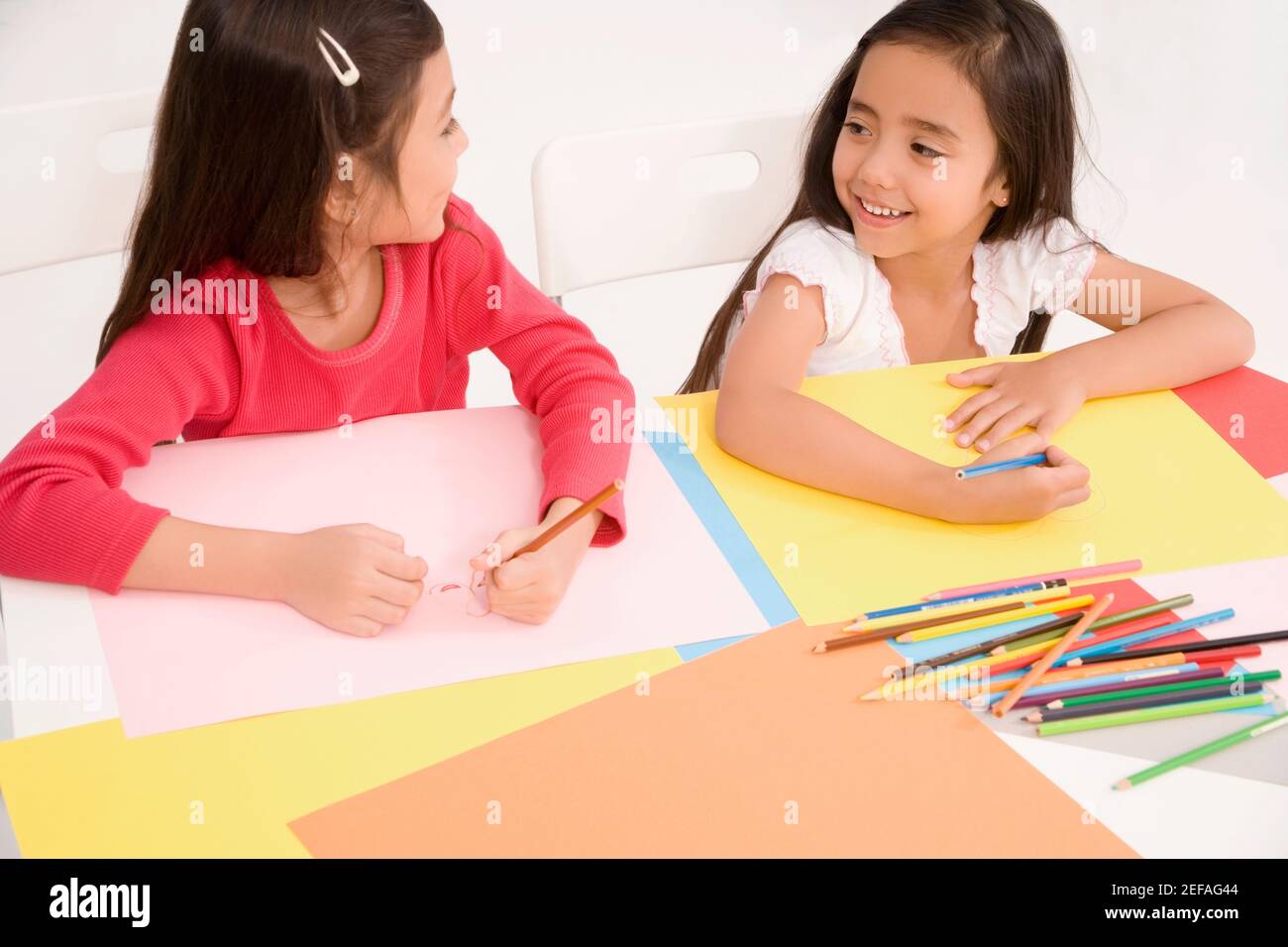 High angle view of two schoolgirls drawing together in a classroom ...