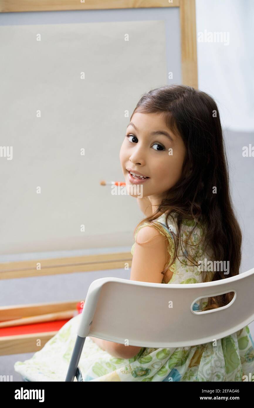 Portrait of a schoolgirl sitting on a chair and painting in an art ...