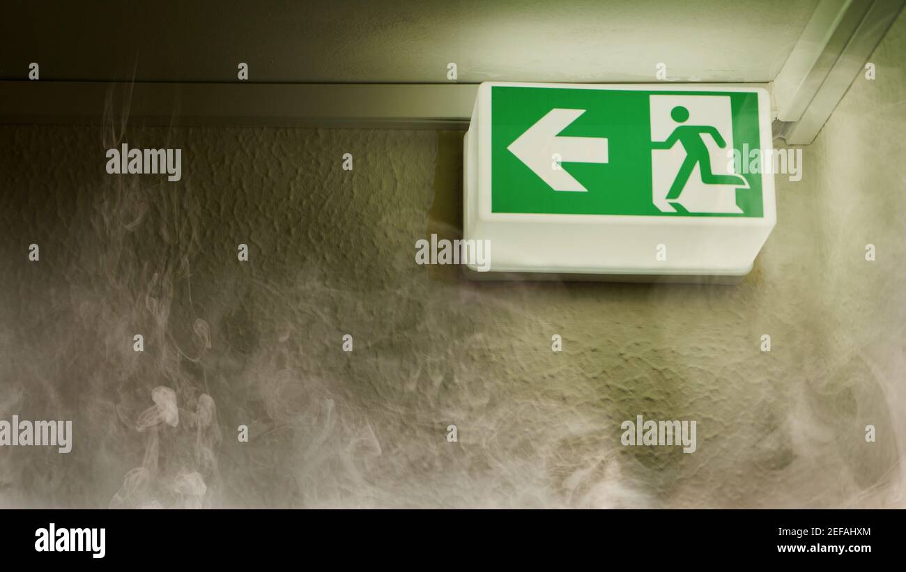 Green glowing emergency exit shows escape route in case of fire with smoke in the house Stock Photo