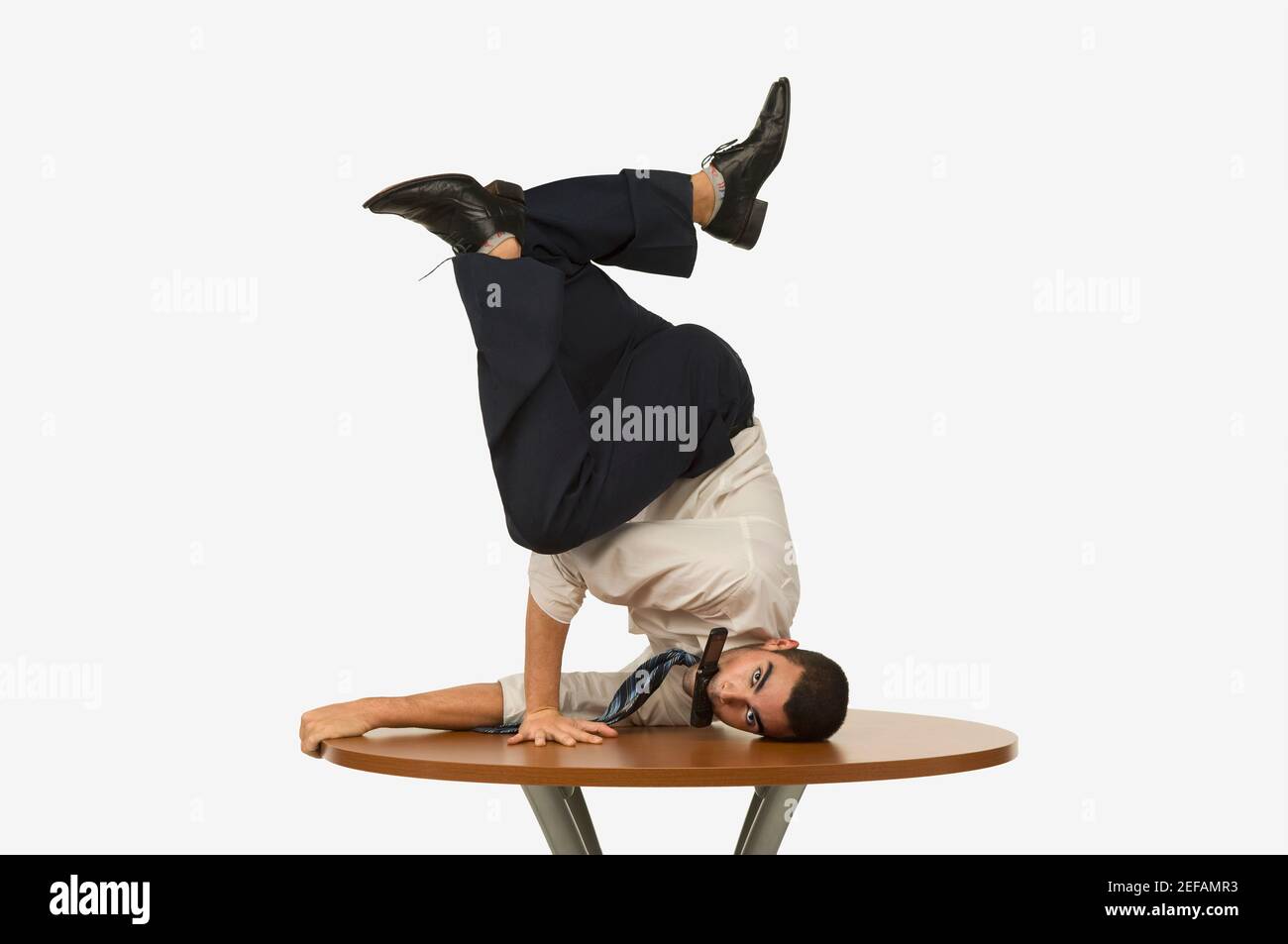 Portrait of a businessman doing a handstand on a table with a mobile phone in his mouth Stock Photo
