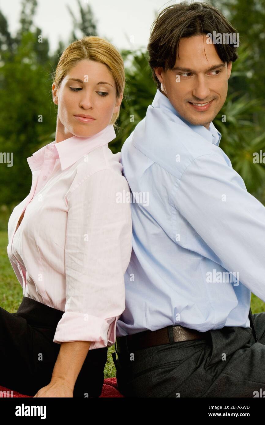 Side profile of a young woman and a mid adult man sitting back to back ...