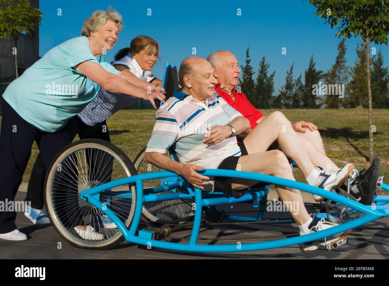 Two senior men sitting on a quadracycle and two senior women pushing it Stock Photo