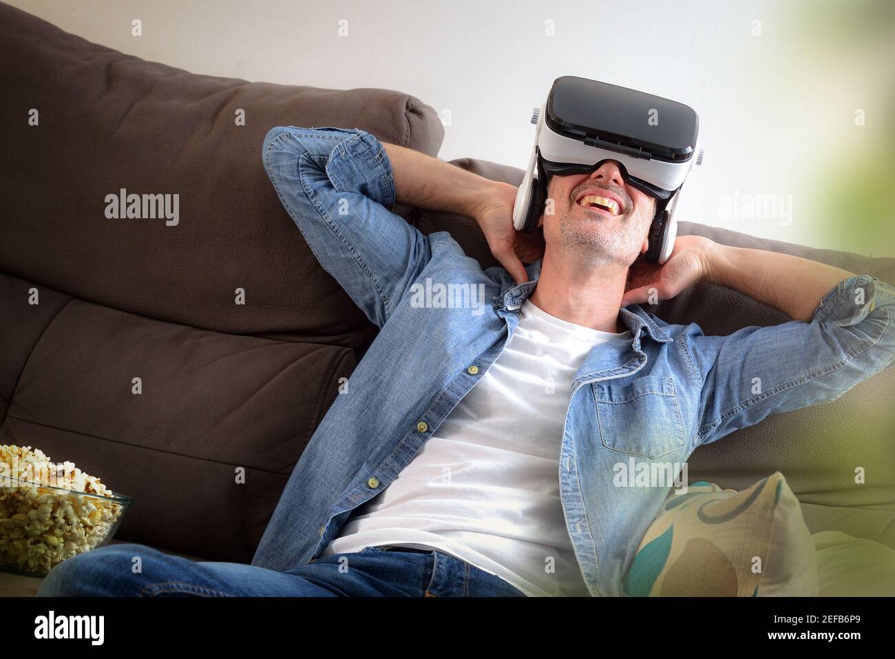 Relaxed entertaining man at home watching movies in virtual reality glasses sitting on the couch with popcorn close up Stock Photo