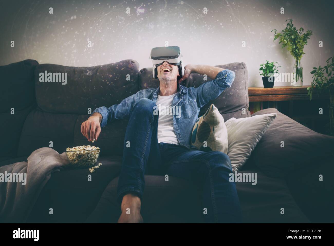 Concept of man watching content in virtual reality glasses eating popcorn on the sofa at home Stock Photo