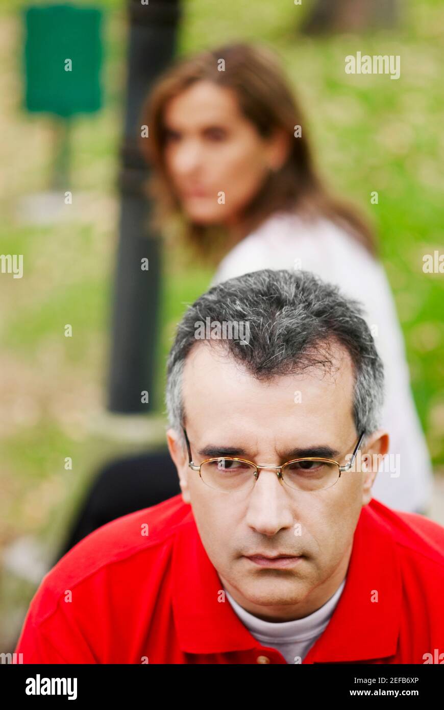 Close-up of a mid adult man looking sad with a mid adult woman sitting behind him Stock Photo