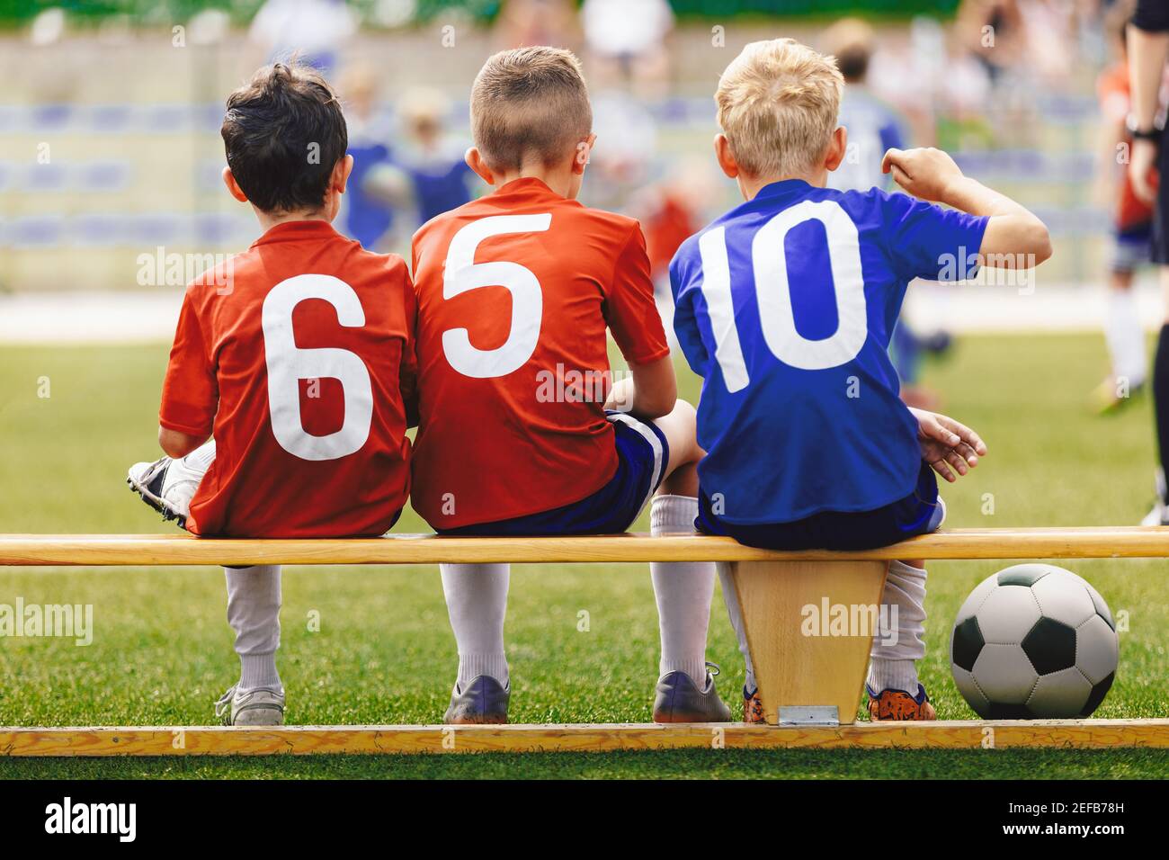 Children in Sports Team. Happy Kids in Sportswear with Ball Sitting on Soccer Football Bench. School Boys Play Sports on Grass Pitch Stadium. Stock Photo