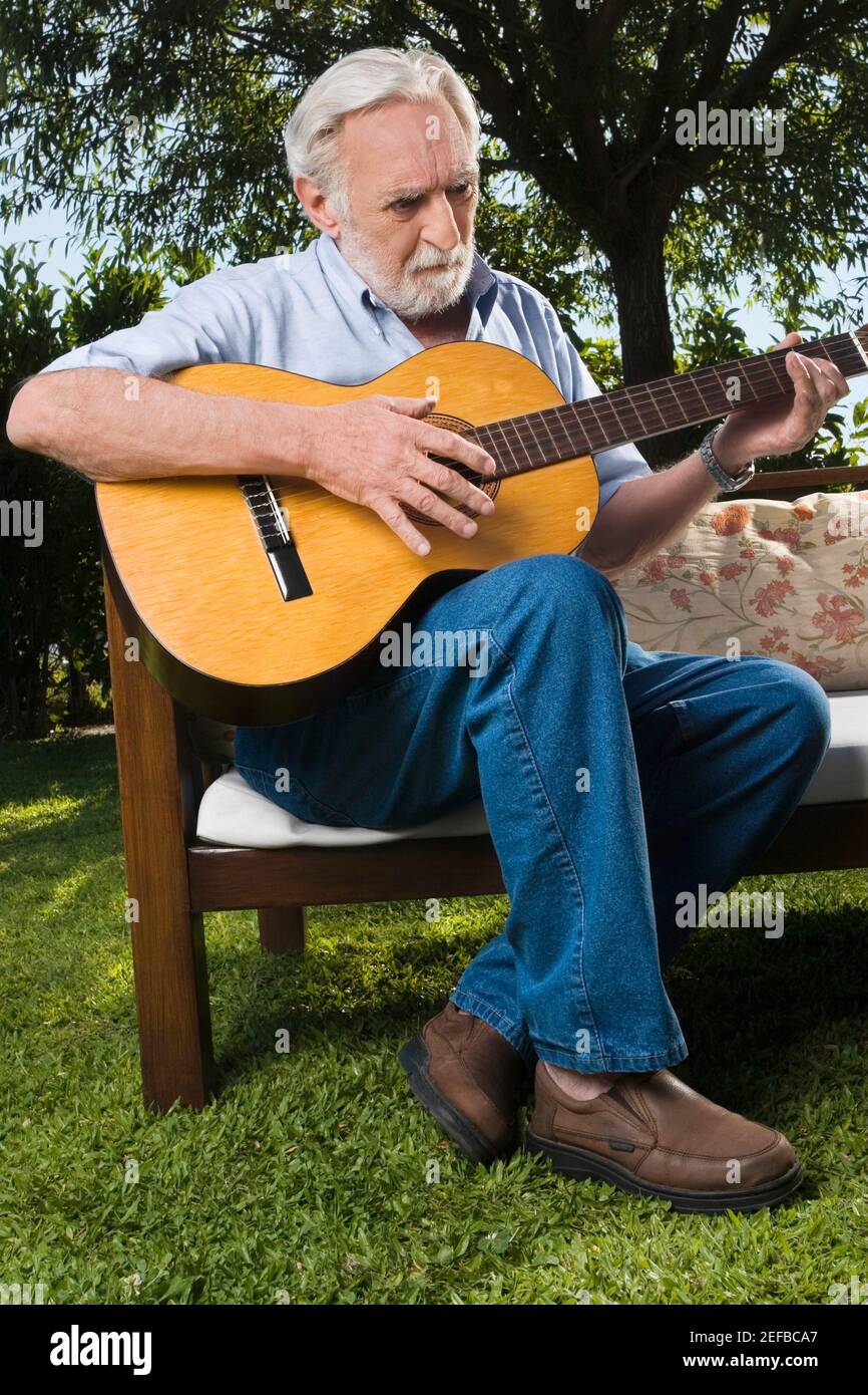 Senior man sitting on a couch and playing a guitar hi-res stock ...