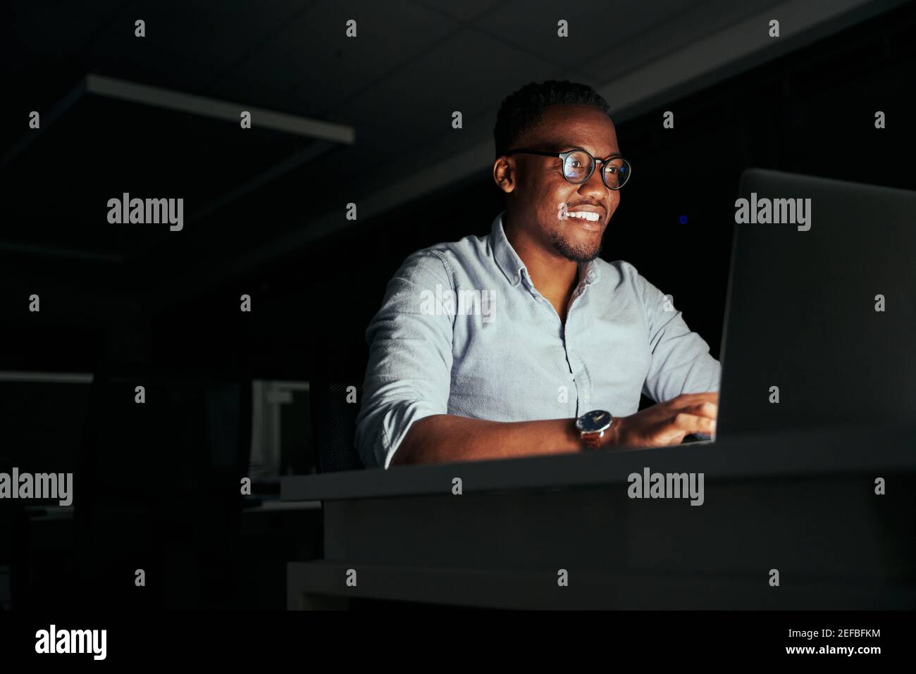 Smiling african young businessman working overtime in the office to finish the project within the deadline Stock Photo