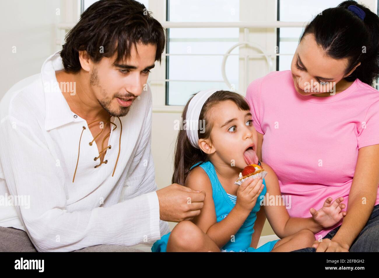 Close-up of a young couple looking at their daughter eating a pastry Stock Photo