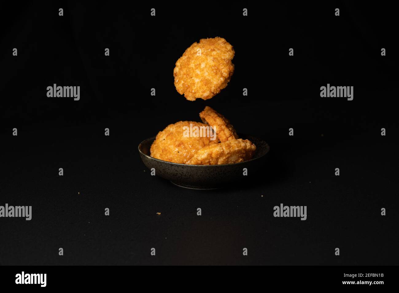 fried crispy rice crackers called rice age with soy,salt sugar etc flavor on black background is a traditional japanese snack. Stock Photo