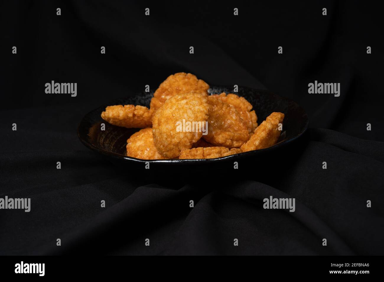 fried crispy rice crackers called rice age with soy,salt sugar etc flavor on black background is a traditional japanese snack. Stock Photo