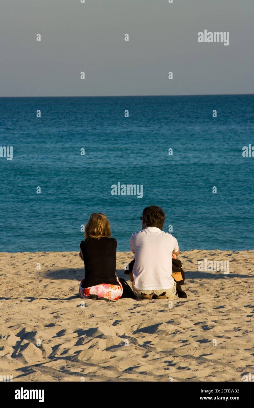 Rear view of a man and a woman sitting on the beach, South Beach, Miami ...