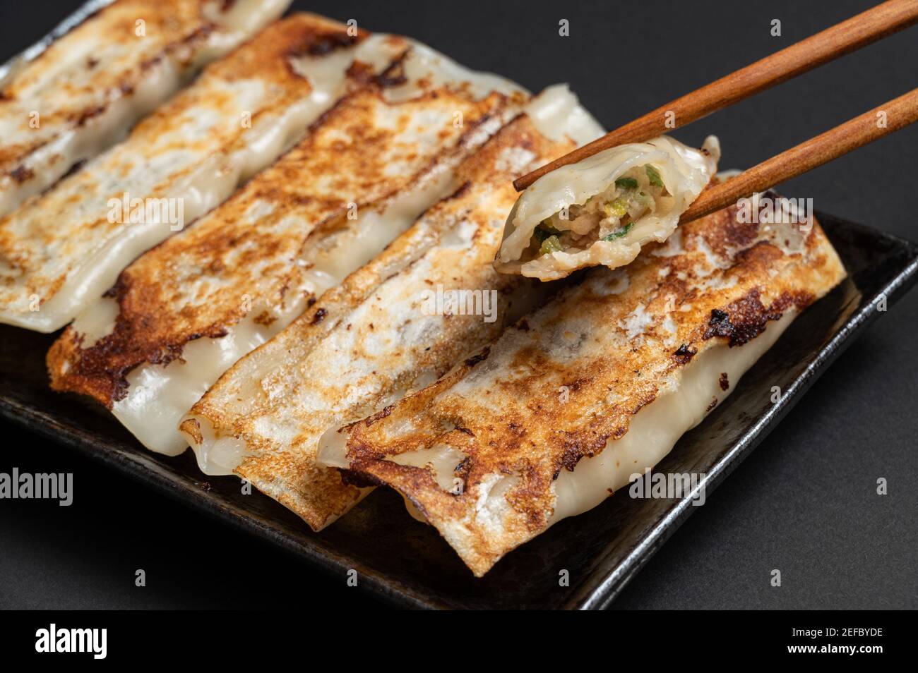 Material of traditional chinese fried dumplings(also called gyoza,pot sticker) on black background with chopsticks. Stock Photo