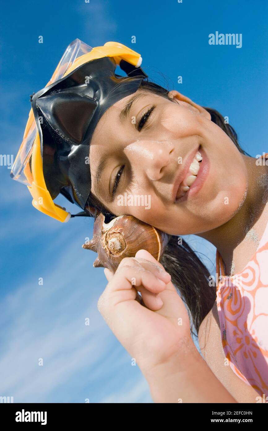 Portrait of a girl wearing a scuba mask and holding a conch shell to her ear Stock Photo