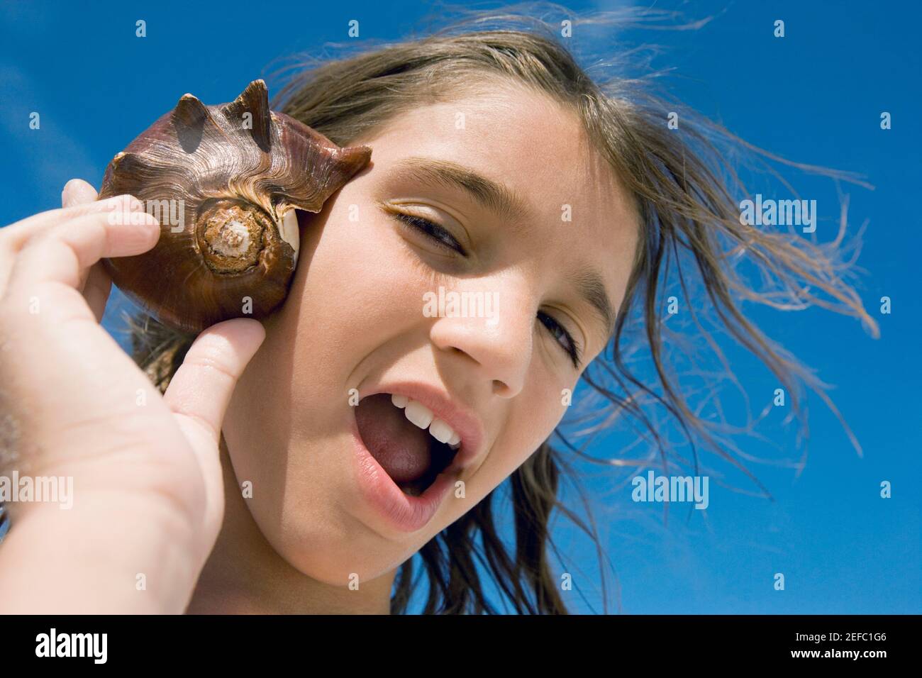 Portrait of a girl holding a conch shell to her ear Stock Photo
