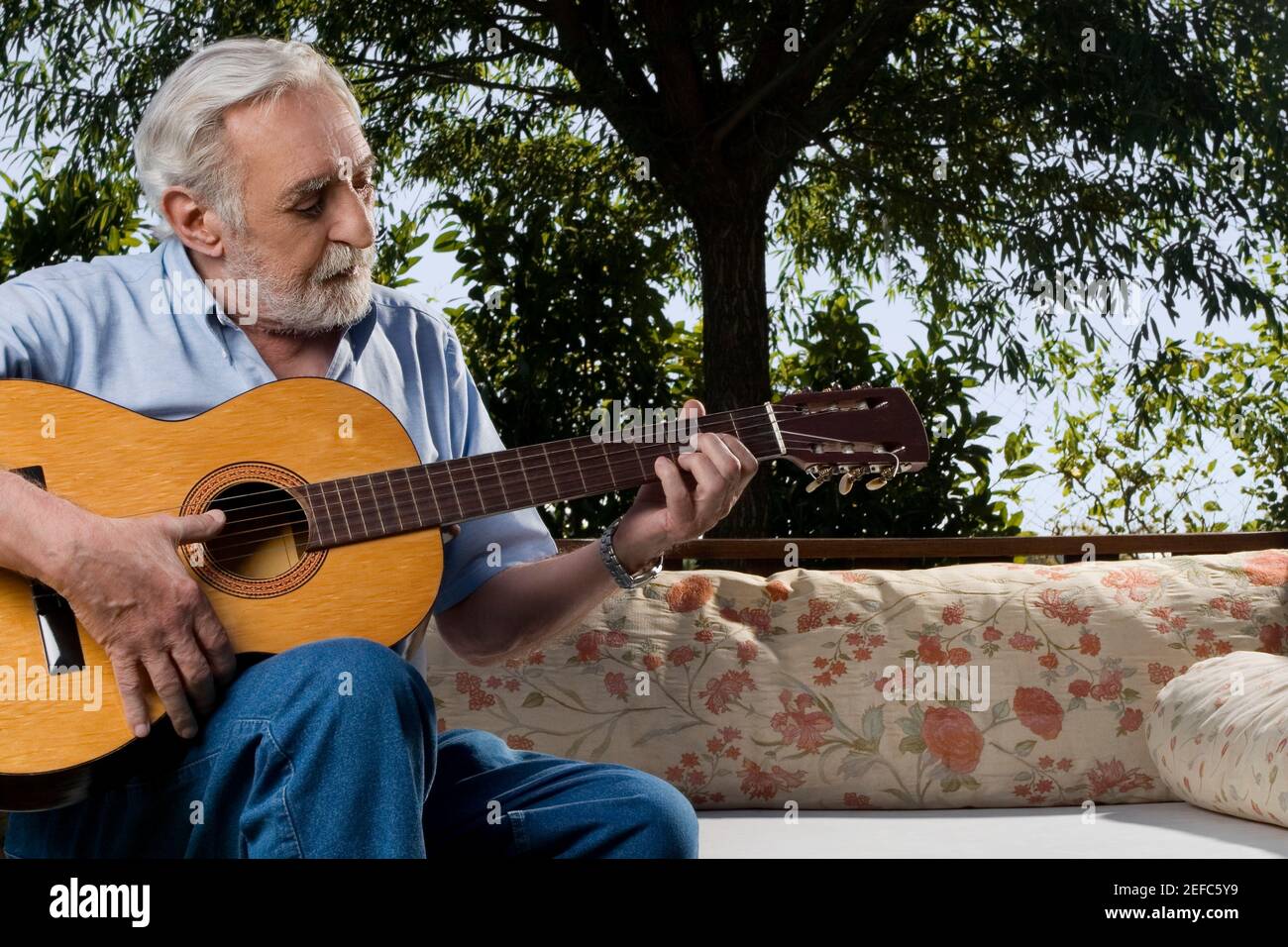 Senior man sitting on a couch and playing a guitar Stock Photo