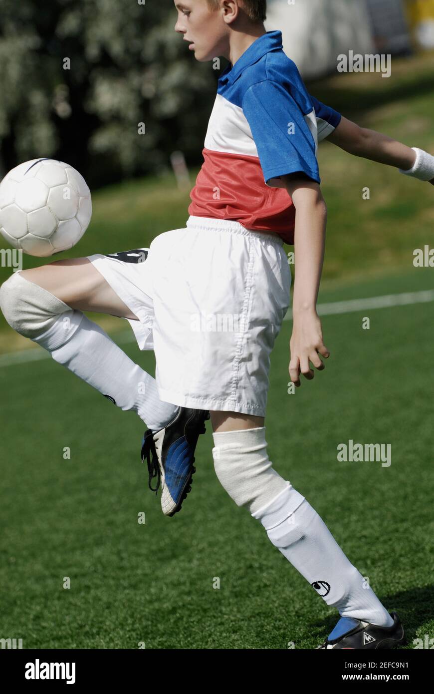 Side profile of a soccer player balancing a soccer ball on his thighs