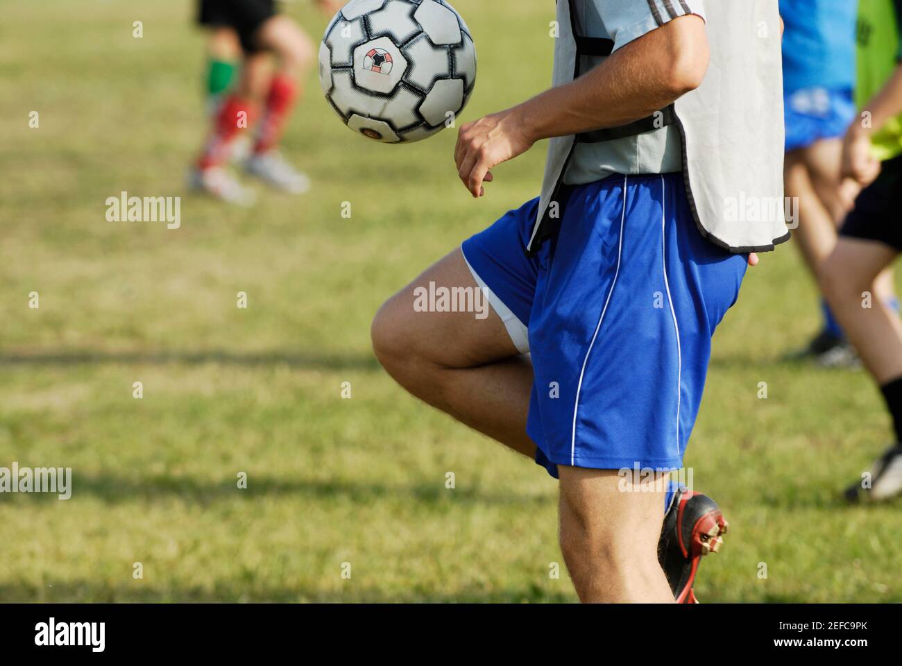 Mid section view of a soccer player balancing a soccer ball on his