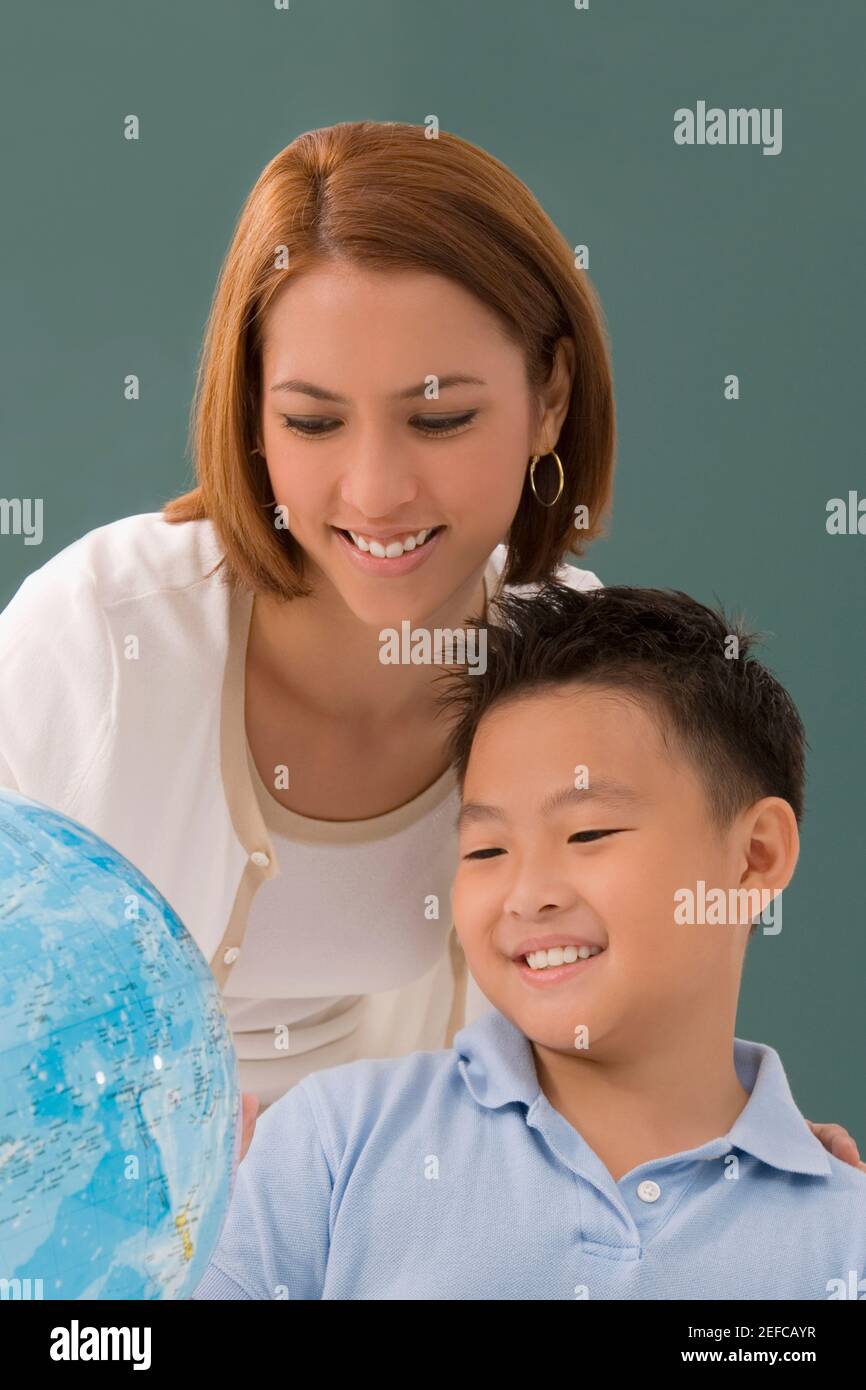 Female teacher with her student looking at a desktop globe and smiling ...