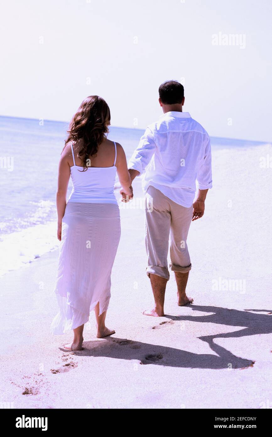 Rear view of a young woman and a mid adult man walking on the beach ...