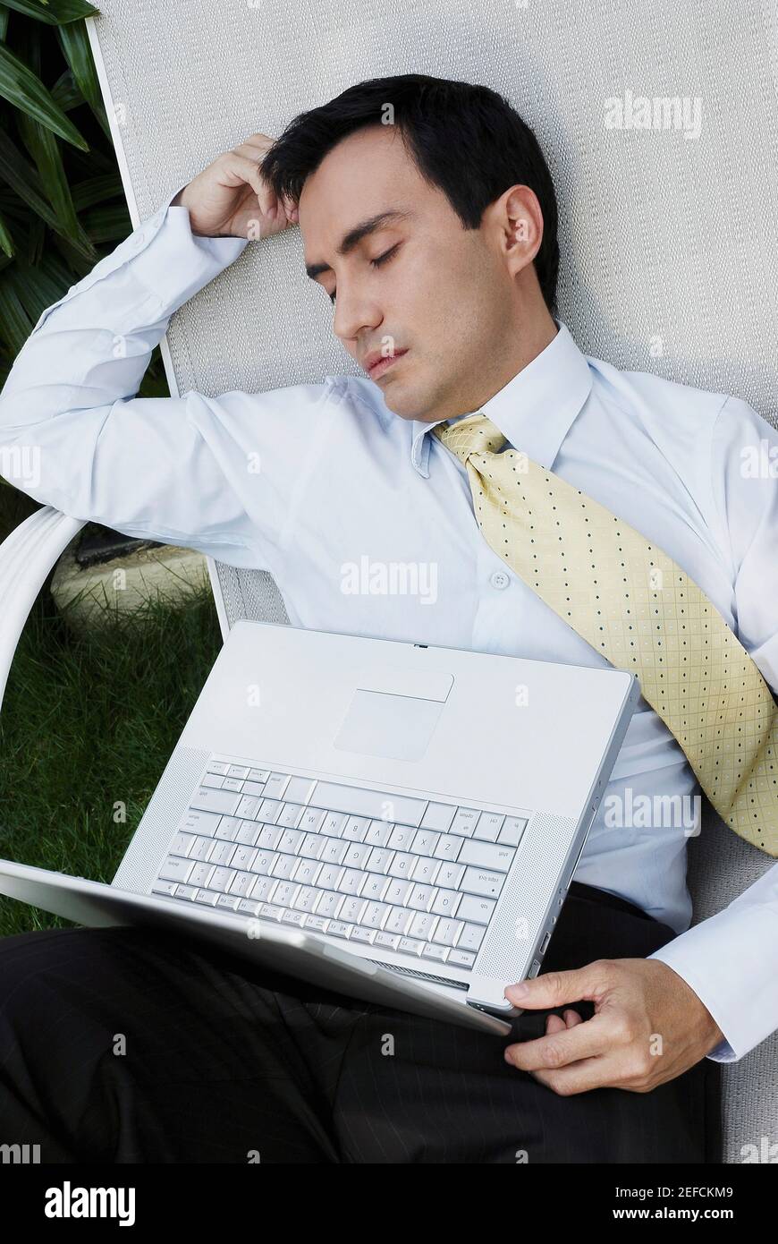 Businessman sleeping on a lounge chair with a laptop on his lap Stock Photo