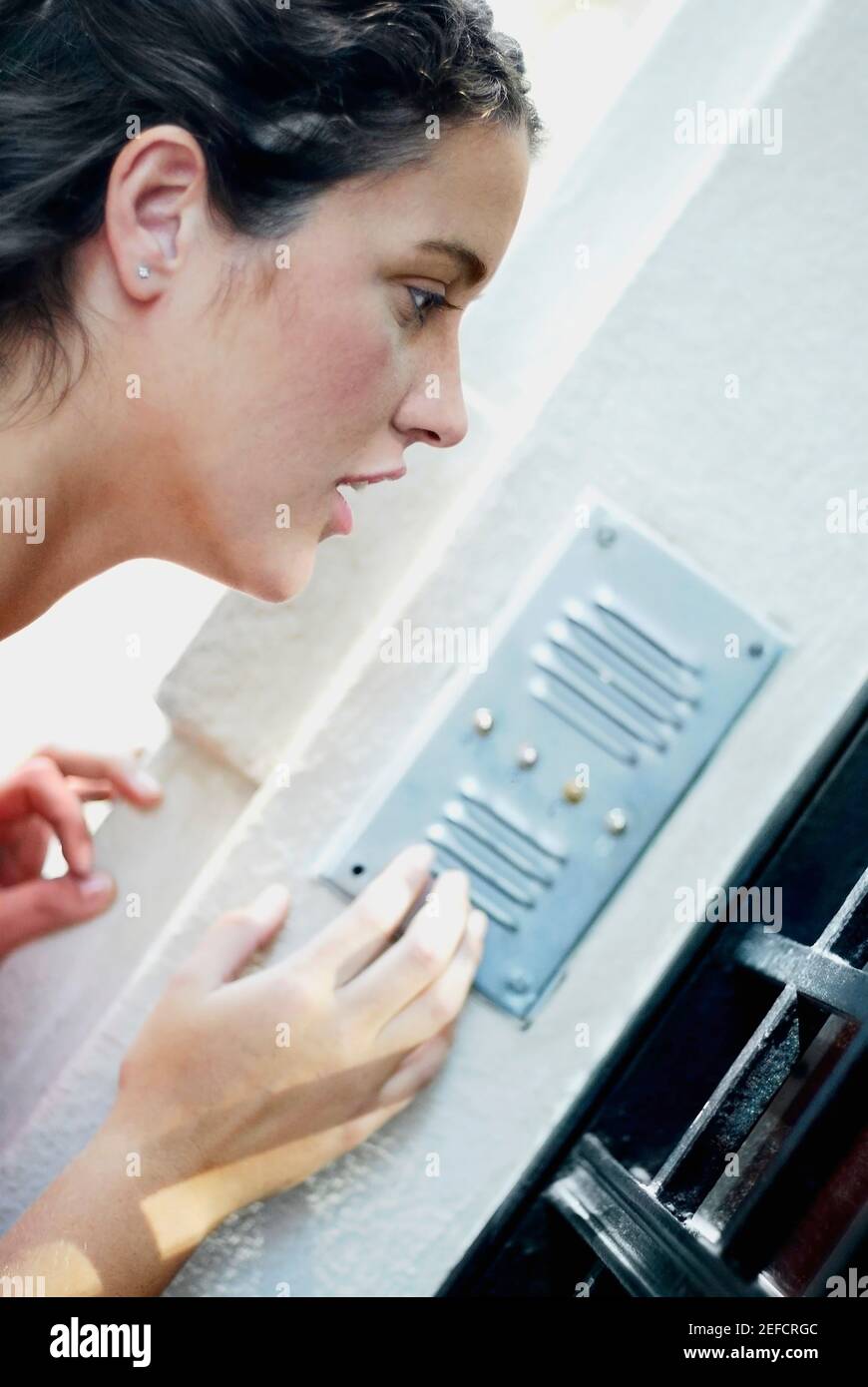 Side profile of a young woman using a doorbell Stock Photo