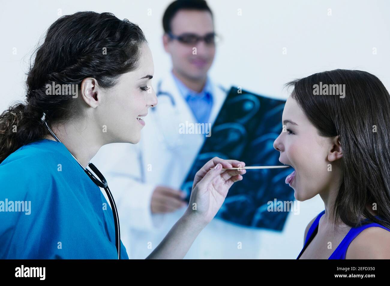 Side profile of a female doctor examining a girlÅ½s mouth with a tongue depressor Stock Photo
