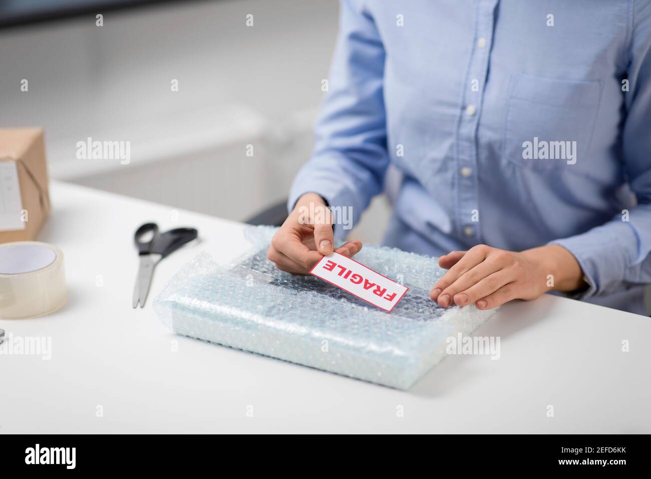 woman sticking fragile mark to wrap at post office Stock Photo