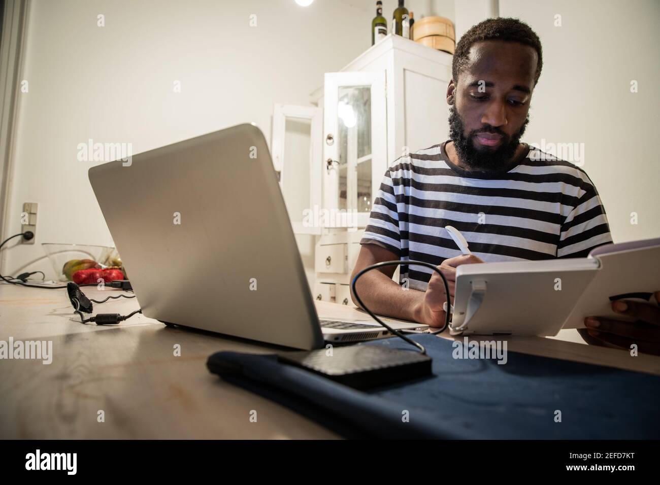 A young male student sitting at the table with is laptop, takes notes on the agenda. Stock Photo