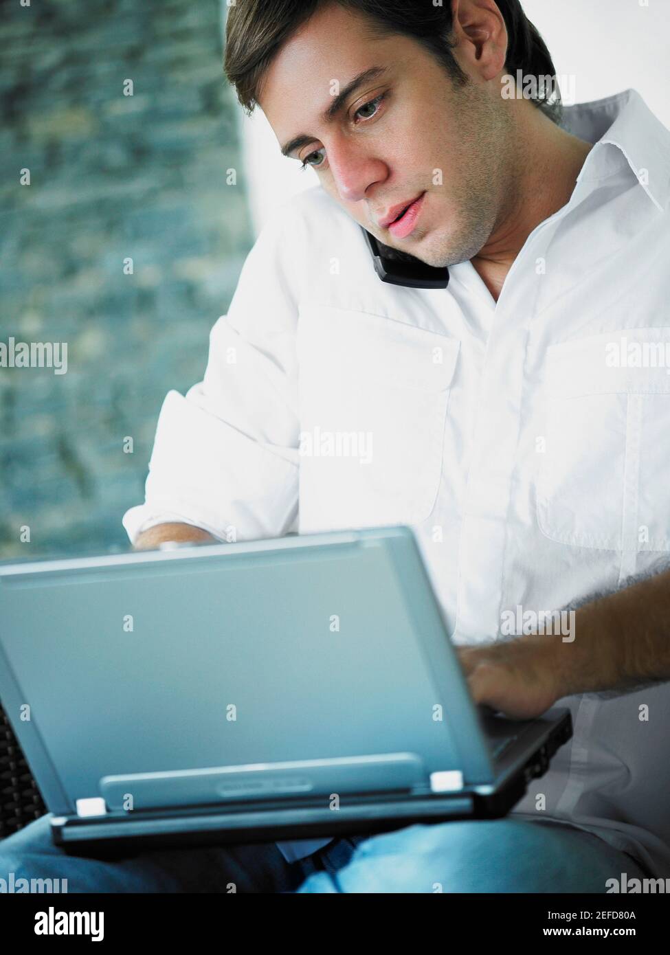 Young man using a laptop while talking on a mobile phone Stock Photo
