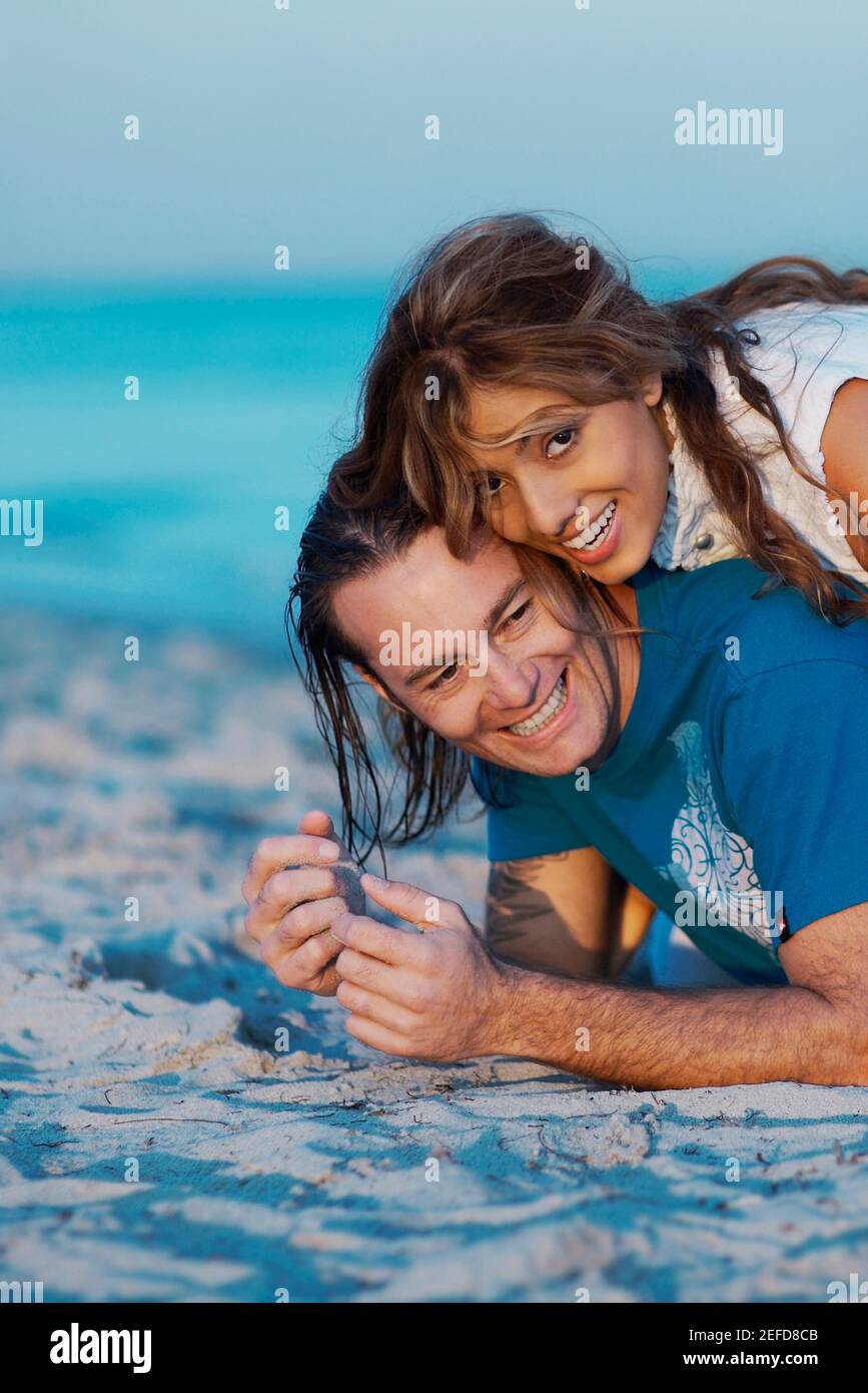 Portrait of a young woman lying on top of a mid adult man on the beach ...